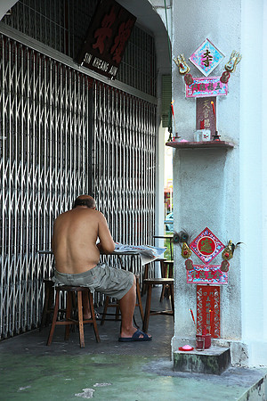 Old man reading new paper at the corridor of the old shop houses in Georgetown